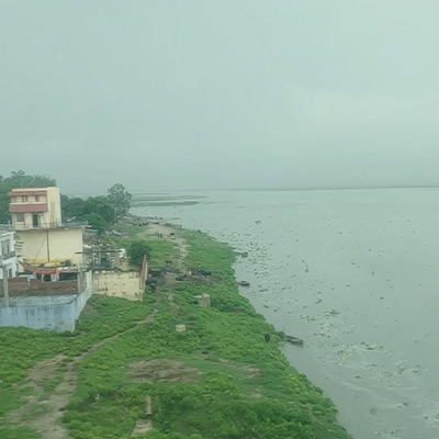 outside-view-from-running-train-crossing-metal-bridge-over-ganga-river-and-village-uttar-pradesh-india